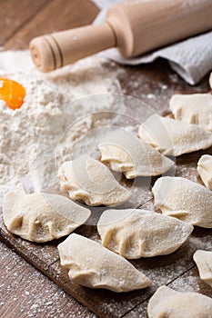 Process of making dumplings, vareniki, pierogi, on wooden board on table with rolling pin, sprinkled with flour and