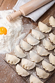 Process of making dumplings, vareniki, pierogi, on wooden board on table with rolling pin, sprinkled with flour and
