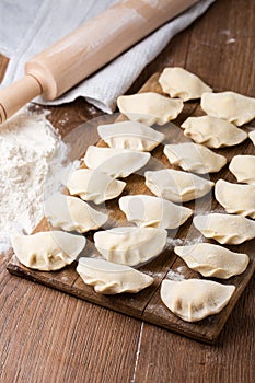 Process of making dumplings, vareniki, pierogi, on wooden board on table with rolling pin, sprinkled with flour. Close