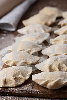 Process of making dumplings, vareniki, pierogi, on wooden board on table, sprinkled with flour. Raw semi finished food