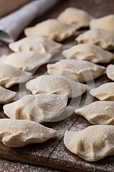 Process of making dumplings, vareniki, pierogi, on wooden board on table, sprinkled with flour. Raw semi finished food