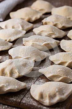 Process of making dumplings, vareniki, pierogi, on wooden board on table, sprinkled with flour. Raw semi finished food