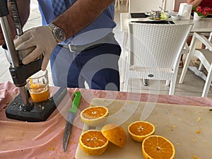 The process of making freshly squeezed yellow orange juice, a man squeezes juice into a glass with his hands in a hotel in a warm