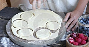 The process of making homemade dumplings. Raw pierogi  with berry on a wooden board with women and child hands