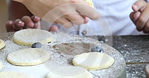 The process of making homemade dumplings. Raw pierogi  with berry on a wooden board with women and child hands