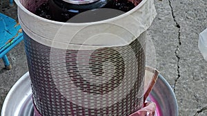 The process of making homemade grape wine. Grapes are pressed in a hydraulic press. Grape juice flows into a container.