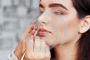 Process of making makeup. Make-up artist working with brush on model face. Portrait of young woman in beauty saloon interior.