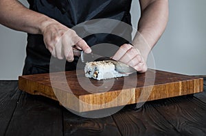 Process of making maki sushi. Cook chef hands preparing rolls with cheese, avocado and sesame seeds on wooden board