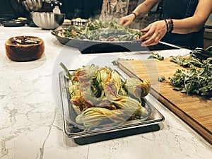 Process of making zucchini flowers. A white woman with bangles on her hands roasts vegetables in the kitchen. Marble background