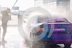 Process of man washing his car in a self-service car wash station. Back view