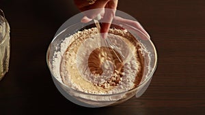 the process of mixing healthy ingredients to prepare vegan blueberry muffins in a glass bowl.