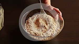 the process of mixing healthy ingredients to prepare vegan blueberry muffins in a glass bowl.