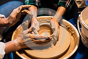 The process of modeling clay dishes on a Potter`s wheel, the hands of a young girl and a child.