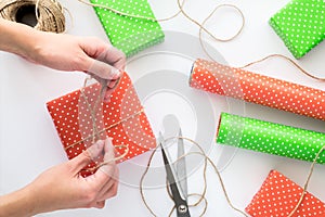 Process of package and wrapping Christmas and New Year gift box with woman hands. Wrapping paper, scissors, twine on the white bac
