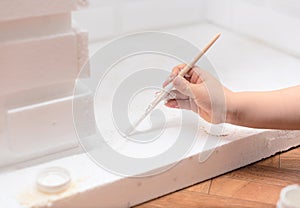 Process of painting a decorative fireplace with hand holding a brush with white paint gouache close up. Home improvement