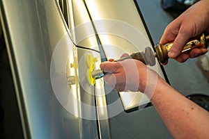 Process Of Paintless Dent Repair On Car Body. Technician s Hands With Puller Fixing Dent On Rear Car Fender. PDR Removal photo