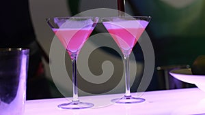 The process of preparation of a cocktail, the barman in two beautiful glasses on high legs with a prepared drink pours