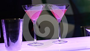 The process of preparing a cocktail, the barman in two beautiful glasses on high legs pours a cocktail from a shaker