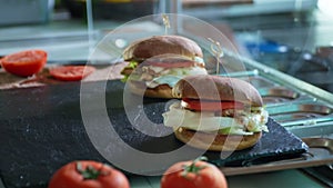 Process of preparing fresh juicy burger with tomato, lettuce and grilled meat with cheese on a black board, fast food