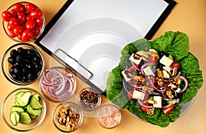 The process of preparing Greek salad. Healthy food concept. On the table is a tablet with a sheet of paper, Greek salad and