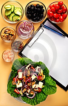 The process of preparing Greek salad. Healthy food concept. On the table is a tablet with a sheet of paper, pen, Greek salad and