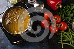 The process of preparing Italian pasta, cooked in a saucepan, against a background of vegetables and spices