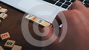 Process of putting together words YES and NO made of wooden blocks with multicoloured letters next to the laptop closeup