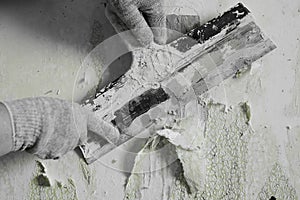 The process of removing old worn out unattractive green from the wall with the help of available tools and a spatula, hands,