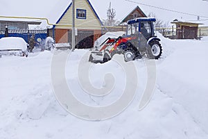 Process of removing snow mechanically with a small blue tractor with a red boom and an excavator bucket. Winter work to ensure the photo