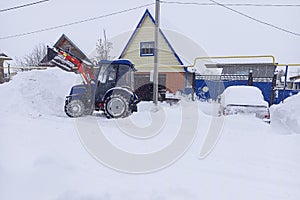 Process of removing snow mechanically with a small blue tractor with a red boom and an excavator bucket. Winter work to ensure the photo