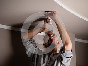 The process of replacing a damaged LED lamp with a downlight. A man in the dark repairs a ceiling soffit