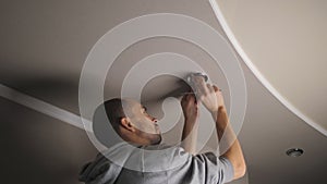 The process of replacing an LED lamp with a downlight. A man in the twilight repairs a ceiling soffit