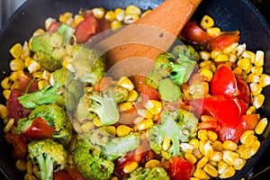 Process of steames vegetables cooking. Colourful vegetables are being mixed in a pan by wooden spatula.