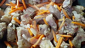 Process of stewing fried pork pieces with carrot strips and onions. Close-up of food preparation