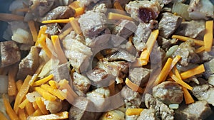 Process of stewing fried pork pieces with carrot strips and onions. Close-up of food preparation