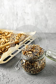 The process of storing homemade granola. A glass jar, a wooden spoon and a baking tray with a dry breakfast on the