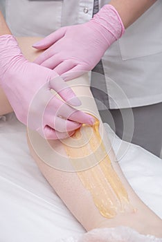 The process of sugar depilation. Master in medical gloves puts a yellow paste on the client`s leg