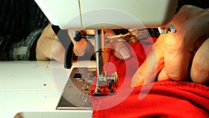 Process of tailoring working, hands of elderly seamstress sews clothes of red cloth with needle.