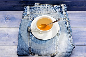 Process tea brewing in ceramic mug. Herbal green or black whole leaf. Mug filled boiling water and tea bag on blue jeans