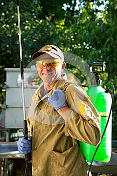 The process of treating plants with pesticides. A farmer in goggles, gloves and work clothes smiles and holds a pollinator in his