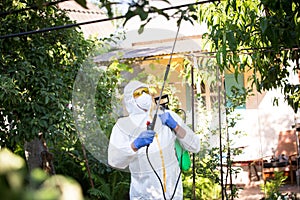 The process of treating plants with pesticides. Farmer in protective suit and mask walking trough orchard with pollinator machine