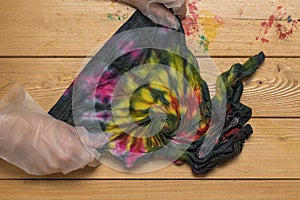 The process of unfolding a T-shirt painted in tie dye style. Flat lay