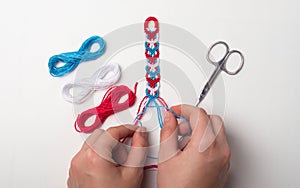 Process of weaving knot for DIY friendship bracelet. Female hands. White background with copy space, scissors and thread