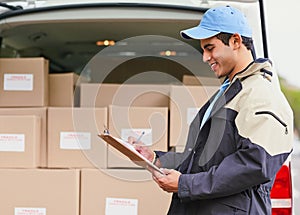 Processing his deliveries for the day. a delivery man writing on a clipboard while standing next to a van full of boxes.