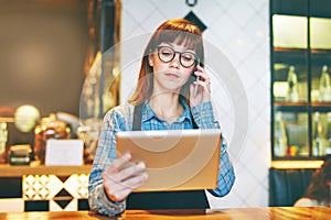 Processing orders the smart way. a young business owner using a digital tablet while talking on a cellphone in her cafe.