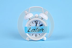 Procrastination, delay, urgency concept. White alarm clock with a sticky note with text later