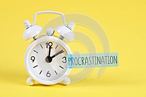 Procrastination, delay, urgency concept. White alarm clock with text procrastination