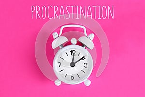 Procrastination, delay, urgency concept. White alarm clock with text procrastination