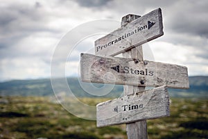 Procrastination, steals and time text on wooden sign post outdoors in landscape scenery.