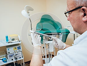 Proctologist holding an anoscope against a proctological chair.
